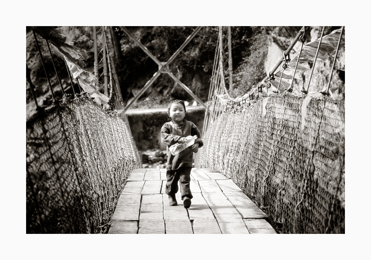 Fine art image of a boy with a plastic bottle crossing a bridge from the '90s, Nepal.