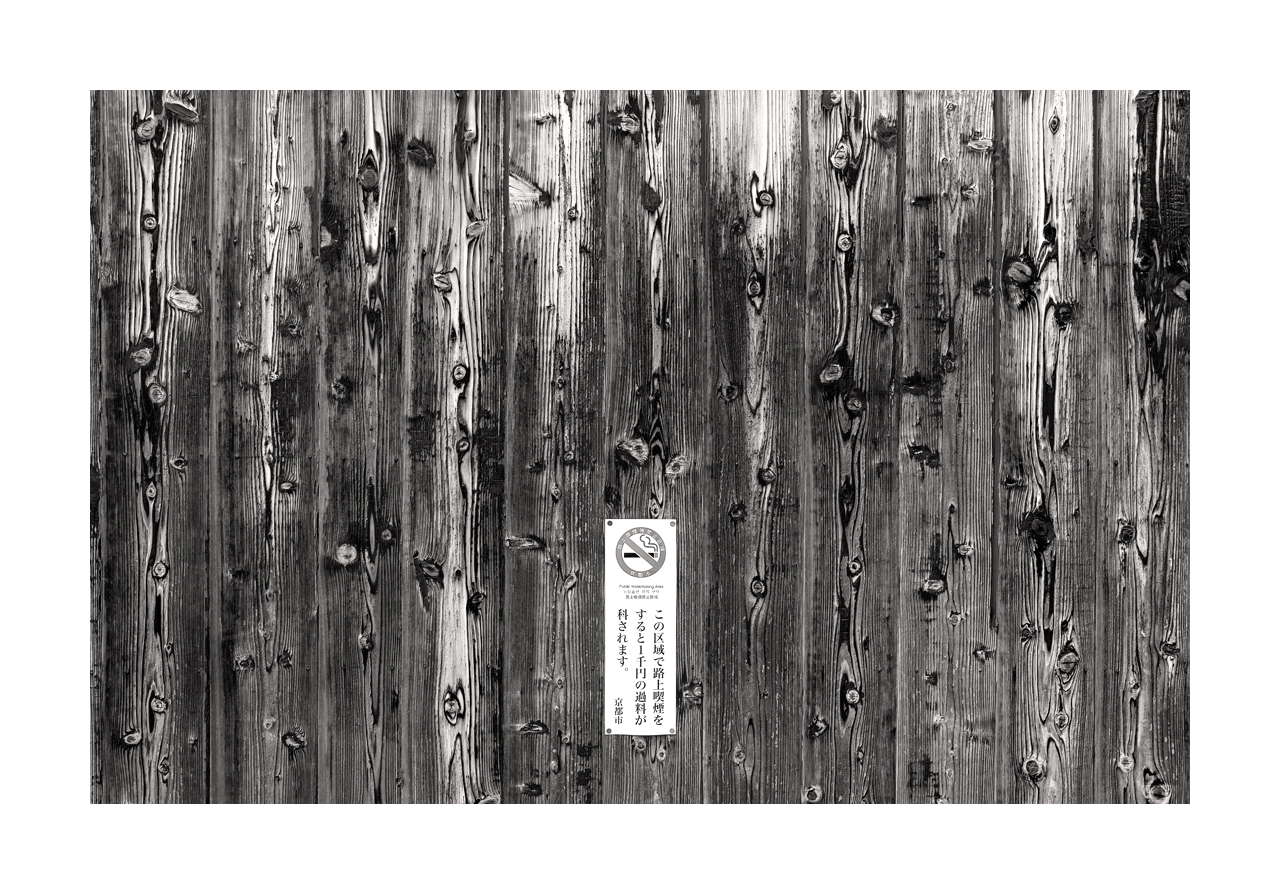Fine art black and white image of a wooden fence with pronounced grain and no smoking warning sign.